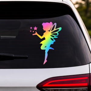 May include: A colorful fairy sticker with a gradient of pink, yellow, green, and blue. The fairy has wings and is holding three stars. The sticker is applied to the rear window of a vehicle.