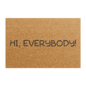 Puede incluir: Una alfombra de puerta rectangular con una superficie texturizada de color marrón claro. El texto "HI, EVERYBODY!" está impreso en letras estilizadas de color gris oscuro en el centro de la alfombra. Esta alfombra de bienvenida está diseñada para una entrada.