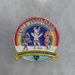 May include: A round enamel pin featuring three cartoon characters against a rainbow backdrop. The pin has the text "ICE PICK PALS" and "CREATING GOLD MEDAL FRIENDSHIP". The characters include a bunny, a llama, and a creature with a pink head.