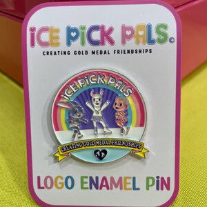 May include: A logo enamel pin featuring the text "ICE PICK PALS" and three cartoon characters. The pin has a white background with a pink border and the text "CREATING GOLD MEDAL FRIENDSHIPS".