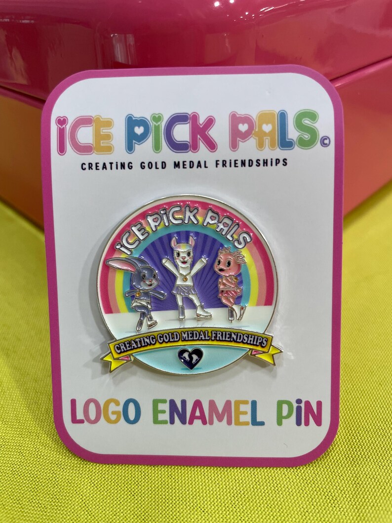 May include: A logo enamel pin featuring the text "ICE PICK PALS" and three cartoon characters. The pin has a white background with a pink border and the text "CREATING GOLD MEDAL FRIENDSHIPS".
