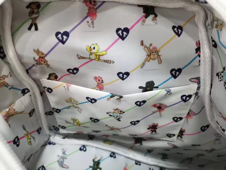 May include: White tote bag interior with a whimsical pattern of cartoon characters, hearts, and colorful lines. The lining features a pocket. The bag's interior is visible, showcasing the playful design.