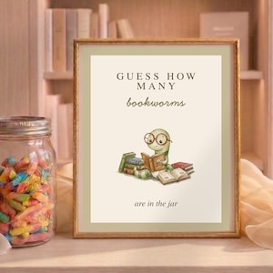 Puede incluir: Un cartel enmarcado con el texto "Guess How Many Bookworms" y una ilustración de un gusano leyendo libros. Un tarro lleno de gusanos de goma de colores está junto al cartel. El fondo incluye estanterías.