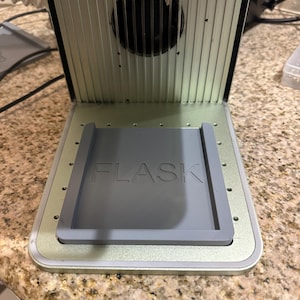 Puede incluir: Una impresora 3D plateada y gris con una bandeja de silicona gris etiquetada "FLASK" en la parte inferior.