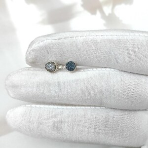 Könnte beinhalten: Ein silberner Ring mit zwei runden, strukturierten, blau-grauen Edelsteinen. Die Edelsteine sind nebeneinander auf dem Ringband angeordnet. Der Ring wird auf einer weißen Oberfläche präsentiert.