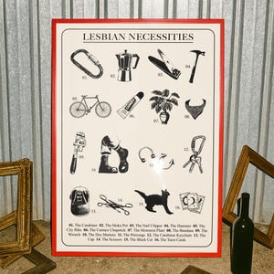 May include: A framed print titled "LESBIAN NECESSITIES" with a red border. The print features 16 black and white illustrations of various items, including a carabiner, a bicycle, a cat, and a pair of scissors. The bottom of the print lists the items.