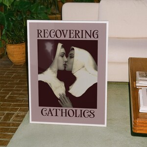 A framed poster featuring two kissing nuns, paired with the text "RECOVERING CATHOLICS."