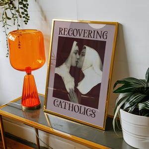 A framed poster featuring two kissing nuns, paired with the text "RECOVERING CATHOLICS."