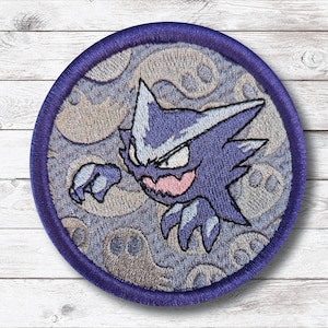 May include: Embroidered patch featuring a purple cartoon character with sharp features and a menacing expression. The character is set against a gray background with ghost-like figures, all within a circular purple border. A fun, decorative item.