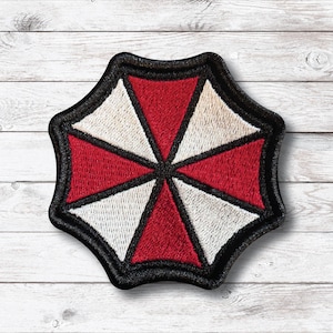 May include: Embroidered patch with a red and white segmented umbrella design, outlined in black. The patch has a detailed, textured finish, ideal for application on clothing or accessories.
