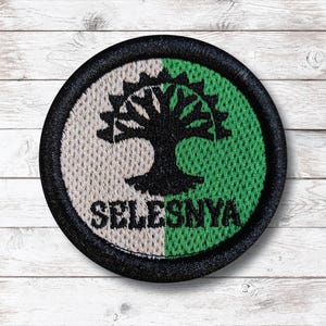May include: Round patch with a black border, featuring a tree design. The patch is divided into two sections: a beige half and a green half. The word "SELESNYA" is printed in white at the bottom of the patch.