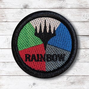 Op de afbeelding: Een ronde patch met een zwarte rand, verdeeld in vier secties van groene, rode, blauwe en grijze mesh. Een zwart embleem staat in het midden en het woord "RAINBOW" is wit geborduurd.