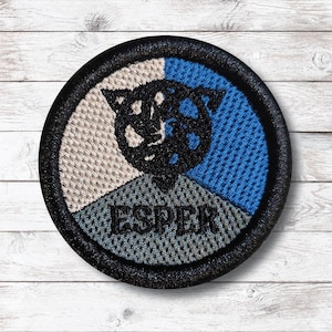 Könnte beinhalten: Gestickter Aufnäher mit schwarzem Rand, mit einem segmentierten Design. Die oberen Abschnitte sind beige und blau, mit einer schwarzen katzenartigen Figur in der Mitte. Der untere Abschnitt ist grau mit dem Wort "ESPER" in Schwarz gestickt.