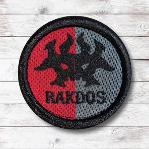 Puede incluir: Parche redondo con borde negro, con un diseño dividido. Una mitad es roja, la otra gris, con un emblema negro en el centro. La palabra "RAKDOS" está impresa en blanco en el lado rojo. El parche tiene una apariencia texturizada.
