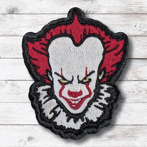 May include: Embroidered patch featuring a menacing clown face with red hair, a white face, and a red nose and mouth. The clown has yellow eyes and a black outline. The patch has a black border and a white, textured background.