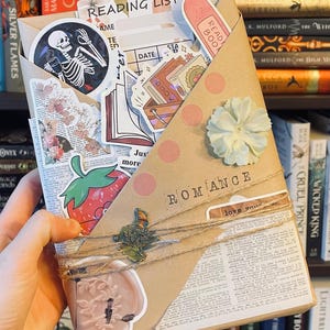 May include: A brown paper package wrapped with twine and decorated with stickers. The package is labelled "Romance" and has a sticker that says "love you".