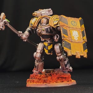 May include: A detailed miniature figure of a heavily armored robot warrior, painted in metallic silver, black, and yellow. The figure is holding a large hammer and a shield with hazard stripes. The base is textured with orange and red tones.