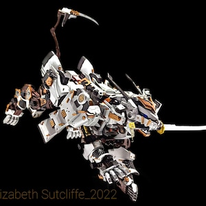 May include: A white and gold detailed robot with a long, curved tail and a sword. The robot has a fierce expression and appears to be in a fighting stance.