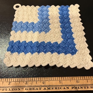 May include: A handmade, square crochet potholder in cream and blue. The design features alternating stripes of cream and blue, with a scalloped edge and a loop for hanging. The potholder is approximately 6 inches wide.