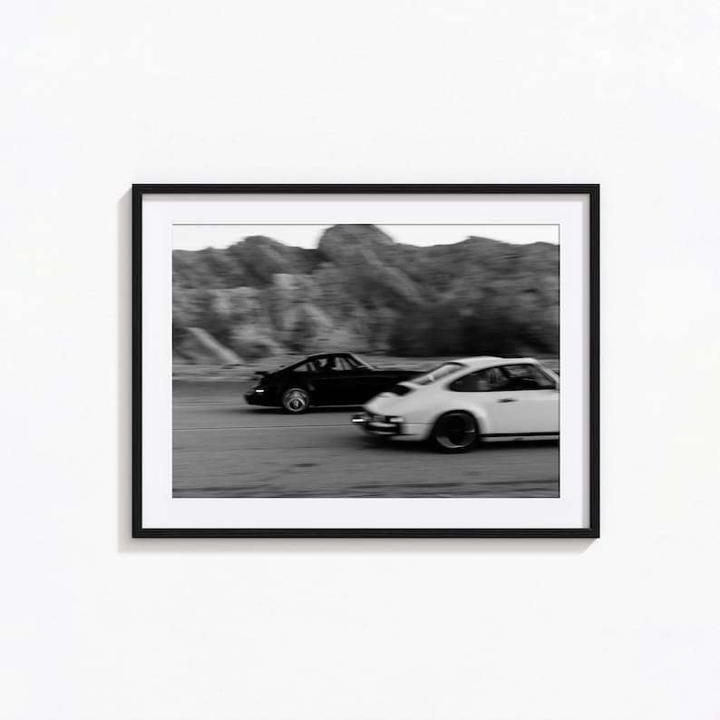 Puede incluir: Impresi&oacute;n enmarcada en blanco y negro con dos coches deportivos compitiendo en una carretera. Un coche es negro, el otro blanco. El fondo muestra monta&ntilde;as borrosas, creando una sensaci&oacute;n de velocidad.