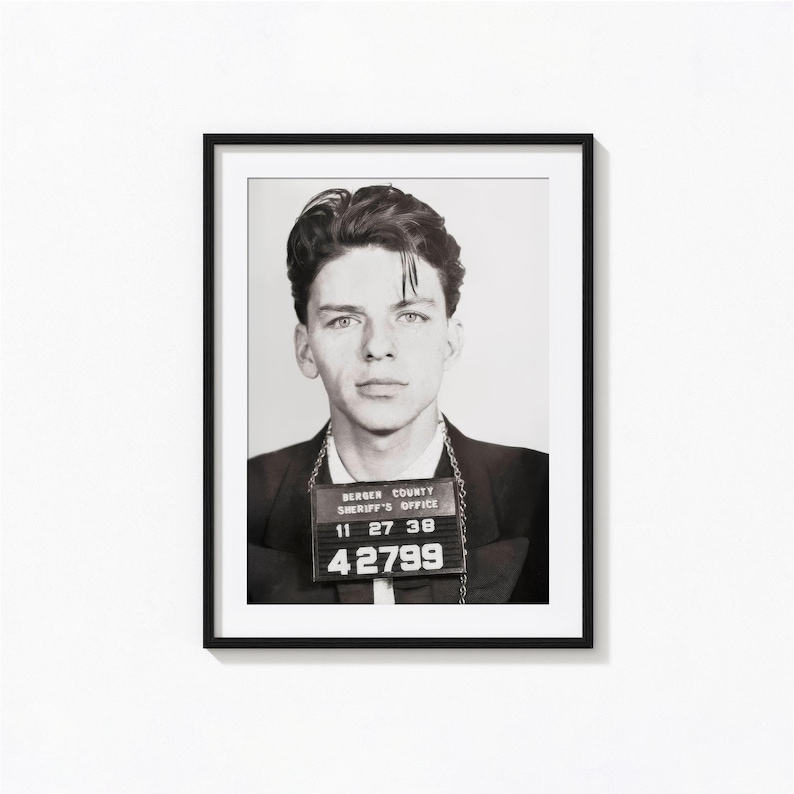 May include: Black and white mugshot of a young man with short dark hair. He is wearing a dark jacket and a chain with a badge that reads "Bergen County Sheriff's Office" and the number "42799".