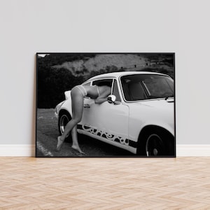 Op de afbeelding: Een zwart-witfoto van een vrouw die in een witte vintage auto leunt. De auto heeft een zwarte race streep met het woord "Carrera" erop.