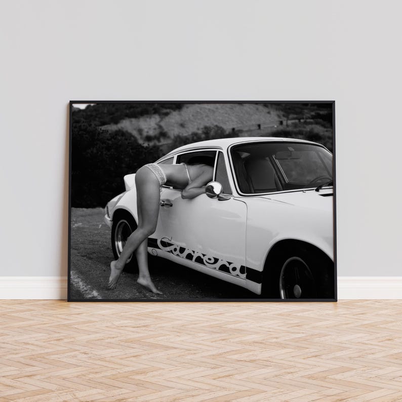 Op de afbeelding: Een zwart-witfoto van een vrouw die in een witte vintage auto leunt. De auto heeft een zwarte race streep met het woord "Carrera" erop.