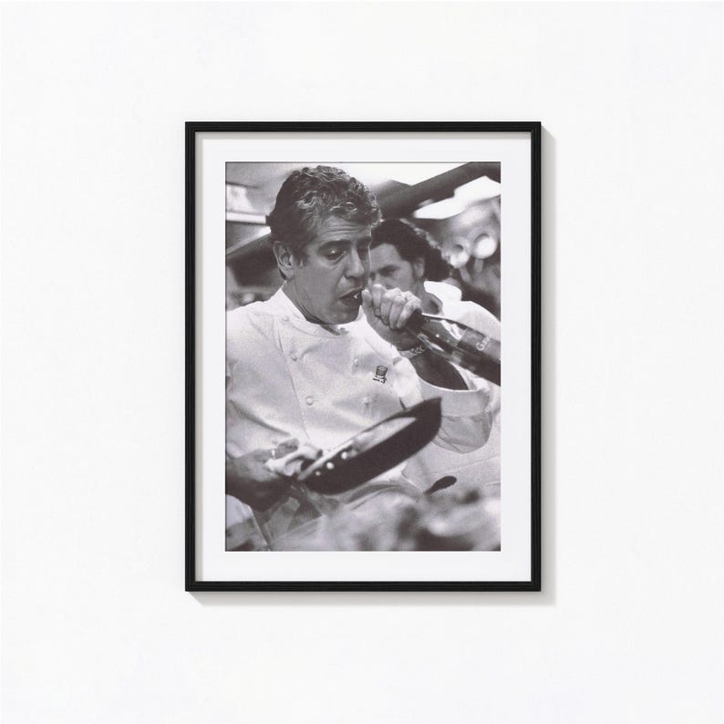 May include: A black and white photograph of a chef in a white chef's coat, holding a frying pan and drinking from a bottle.