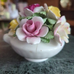 Op de afbeelding: Een wit porseleinen beeldje van een boeket bloemen. De bloemen zijn roze, geel en wit en zijn gerangschikt in een vaas. Het beeldje is een vintage stuk en heeft een delicaat ontwerp.