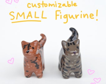 May include: Two small ceramic cat figurines, one brown with black spots and one gray with black stripes. The figurines are standing on a white surface. The text "customizable SMALL Figurine!" is written above the figurines.