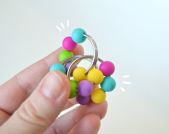 May include: A colorful sensory toy with multiple rings and beads in shades of pink, yellow, green, blue, and purple. The toy is made of metal and silicone.