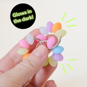May include: A colourful glow-in-the-dark fidget toy with a metal ring and pastel-coloured beads. Glows in the dark!