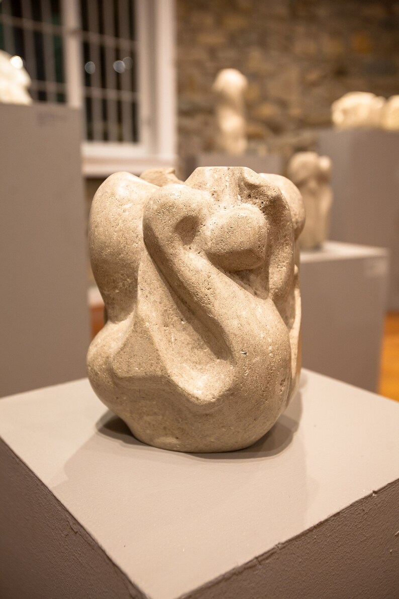 Puede incluir: Una escultura abstracta de cer&aacute;mica blanca con una superficie lisa y texturizada. La escultura se exhibe en un pedestal gris.