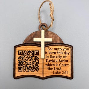Könnte beinhalten: Weihnachtsschmuck aus Holz in Form eines offenen Buches, gekrönt von einem Kreuz. Es zeigt einen QR-Code und den Text "For unto you is born this day in the city of David a Savior, which is Christ the Lord. Luke 2:11."