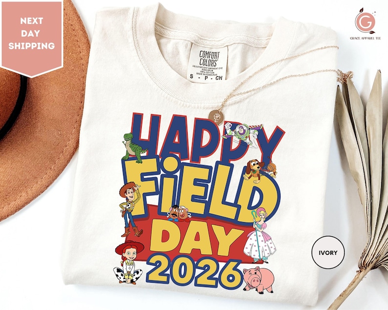 A white t-shirt with a colorful graphic design featuring characters from the Toy Story movie, along with the text "Happy Field Day 2026".