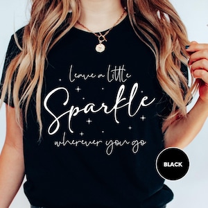 a woman wearing a black t - shirt that says leave a little sparkle wherever you