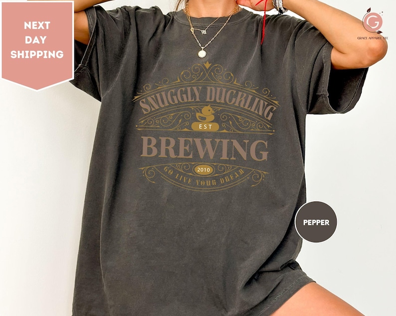 a woman wearing a gray t - shirt with a beer label on it