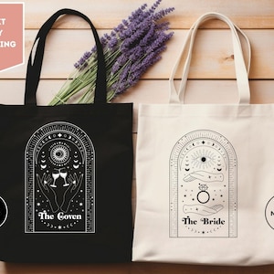 May include: Two tote bags with black and white illustrations of hands holding glasses of wine and a ring. The black bag has the text "The Coven" and the white bag has the text "The Bride".
