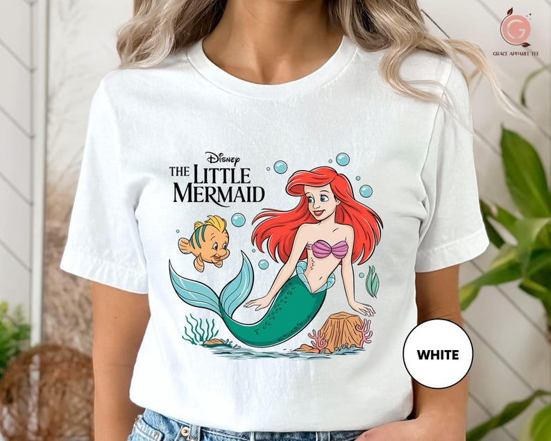 a woman wearing a white shirt with the little mermaid on it