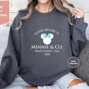 a woman wearing a sweatshirt that says please return to minnie & co main street,