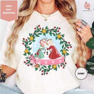 A woman wearing a white t-shirt with a colorful illustration of two women and a snowman.