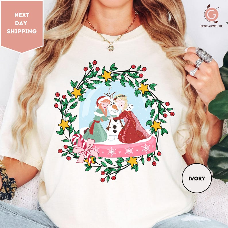 A woman wearing a white t-shirt with a colorful illustration of two women and a snowman.