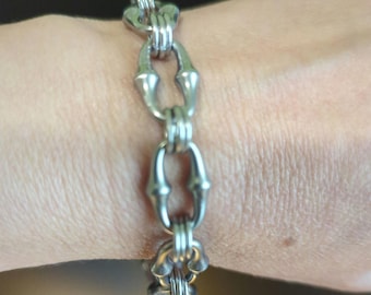 Può includere: Un braccialetto a catena d'argento con un designo unico del collegamento. I collegamenti sono di forma ovale con una piccola barra al centro.