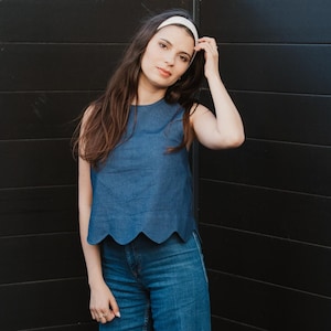 Peut inclure: Un haut sans manches bleu denim avec un ourlet festonné, associé à un jean large assorti. La tenue est complétée par un bandeau blanc. Le modèle se tient devant un mur noir.