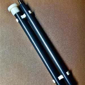 May include: Two black telescopic poles with white plastic end caps and white plastic rings. The poles are extended and lying on a brown surface.