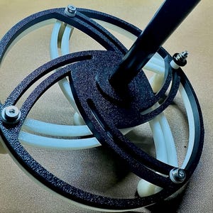 May include: A black and white 3D printed rotating platform with a black metal pole attached to the top. The platform has a textured surface and is designed to rotate smoothly.