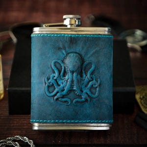 Pode incluir: Uma garrafa de couro azul com tampa prateada e um design de polvo em relevo.