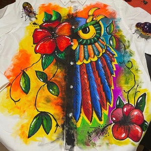 May include: White button-down shirt with a vibrant, hand-painted design. The artwork features a colorful owl with blue, orange, and yellow feathers, surrounded by red flowers and green leaves. The shirt has a unique, artistic flair.
