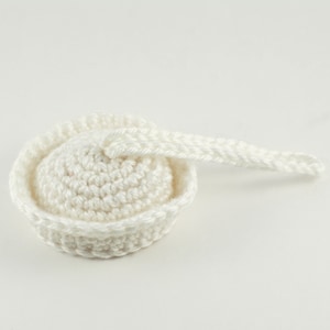 May include: A handmade, off-white crochet item, possibly a hat or a decorative piece. The item features a rounded base with a textured surface and a raised, circular brim. A crocheted chain extends from the top.