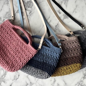 May include: Four crocheted bags with different colored stripes and leather straps. The bags are pink, blue, brown, and gray.